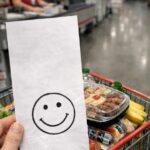 Hand holding a receipt with a hand-drawn smiley face in front of a full shopping cart